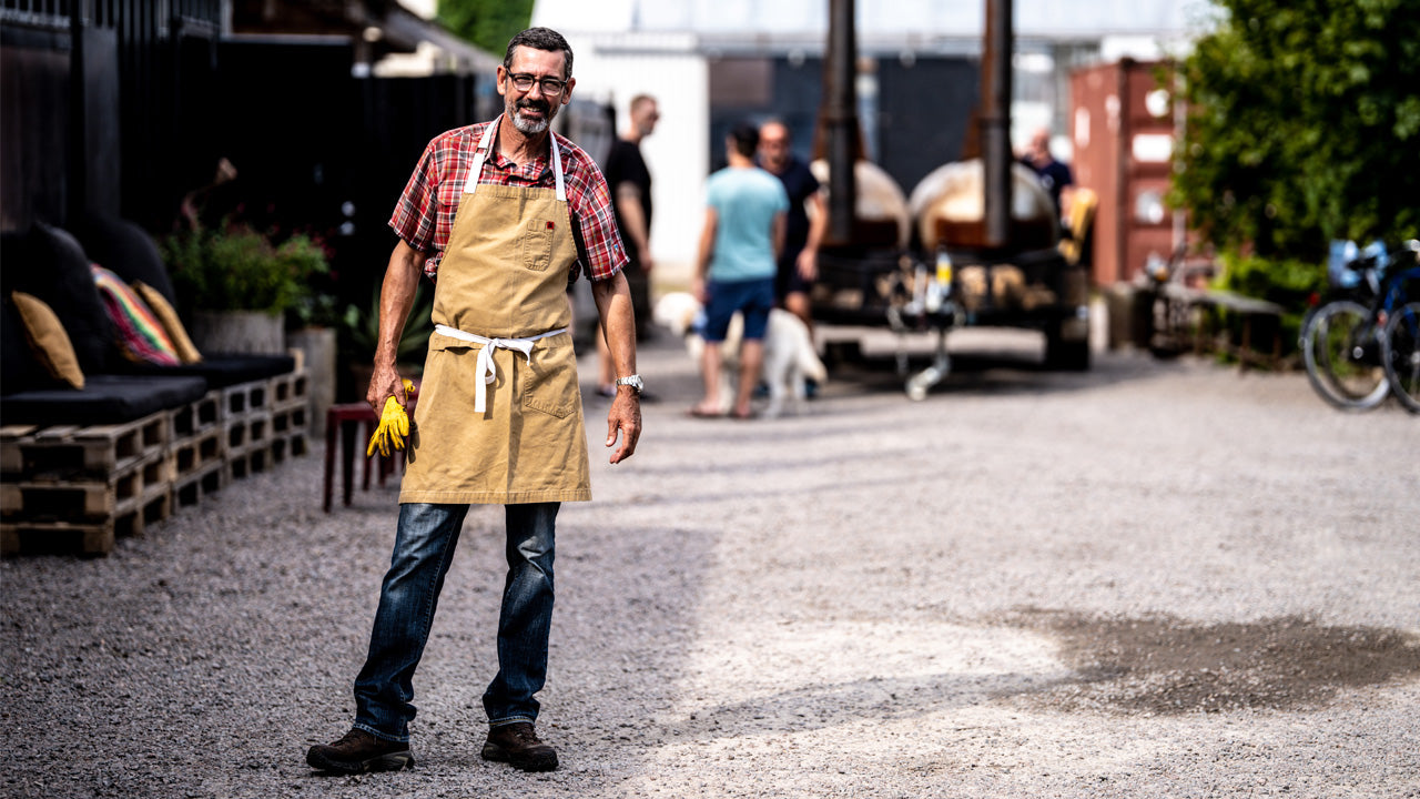 Man wearing a brown apron standing outdoors with blurred background