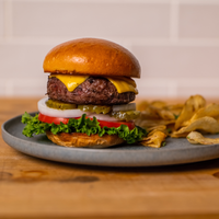 Hamburger with cheese, lettuce, and tomato on a bun, served with chips on a wooden table.