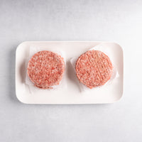 Two raw hamburger patties on a white plate with a light gray background