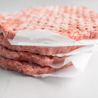 Three raw hamburger patties stacked on top of each other with wax paper in between, on a light gray background.