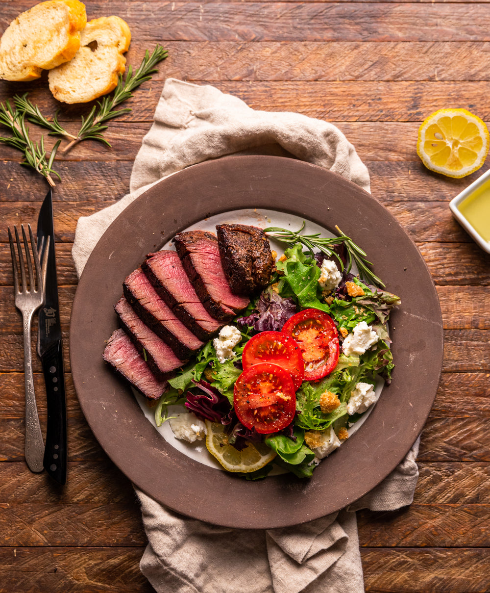 Plated dish of sliced steak with a side salad on a wooden table.