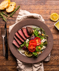 Plated dish of sliced steak with a side salad on a wooden table.