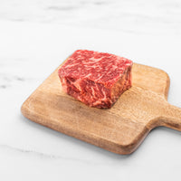 Raw steak on a wooden cutting board with a white marble background