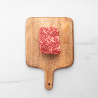 Wooden cutting board with a piece of marbled red meat on a white background