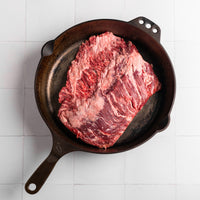 Raw bavette steak in a cast iron skillet on a white tiled surface