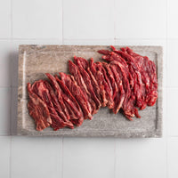Raw beef on a  cutting board with a white tiled background