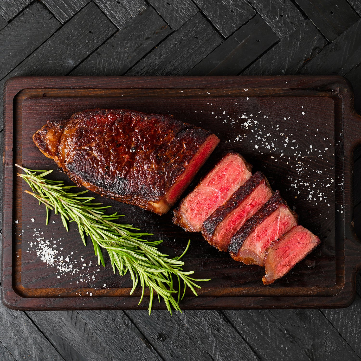 cooked and sliced NY strip steak on cutting board with rosemary sprig and salt |lifestyle