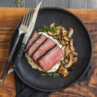 Steak with mushrooms on a black plate with cutlery on a wooden table