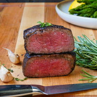 Sliced steak on a wooden cutting board with herbs and a knife