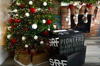 Decorated Christmas tree with ornaments and boxes displaying SRF branding in a room with a brick wall and fireplace.