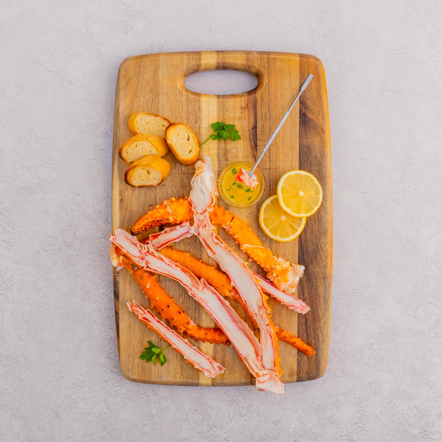 Alaskan Golden King Crab Legs on cutting board with butter dish, lemon slices, and bread