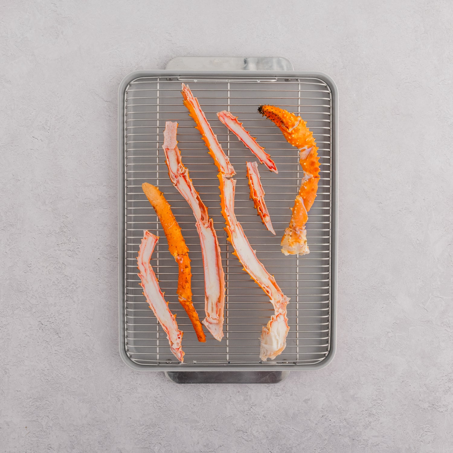 Raw Alaskan golden king crab legs on a metal grilling rack, preparing for cooking.