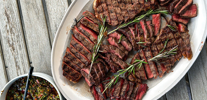 Platter of sliced grilled steak with rosemary on a wooden surface