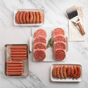 Assorted raw sausages and ground meat on white plates with a spatula on a marble surface.