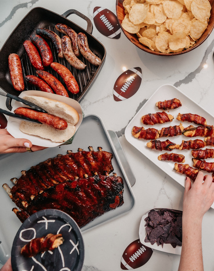 Assorted grilled meats and snacks on a table with football-themed decor.
