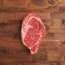 A single bone-in ribeye steak on a wooden surface.