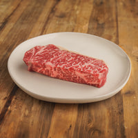 Dry-aged boneless strip steak on white plate 