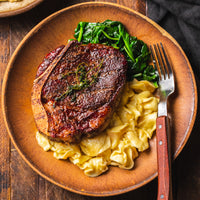 Cooked Bone-In Filet Mignon on plate with pasta and spinach 