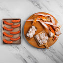 Raw sausages on a metal tray and raw seafood on a wooden board on a marble countertop.