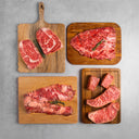 Raw red meat steaks on wooden cutting boards against a gray background