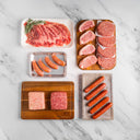Assorted raw meats including steaks, sausages, and ground beef on a marble surface.