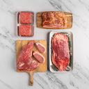 Assorted raw meats on a marble surface including steaks, bacon, and ground beef.