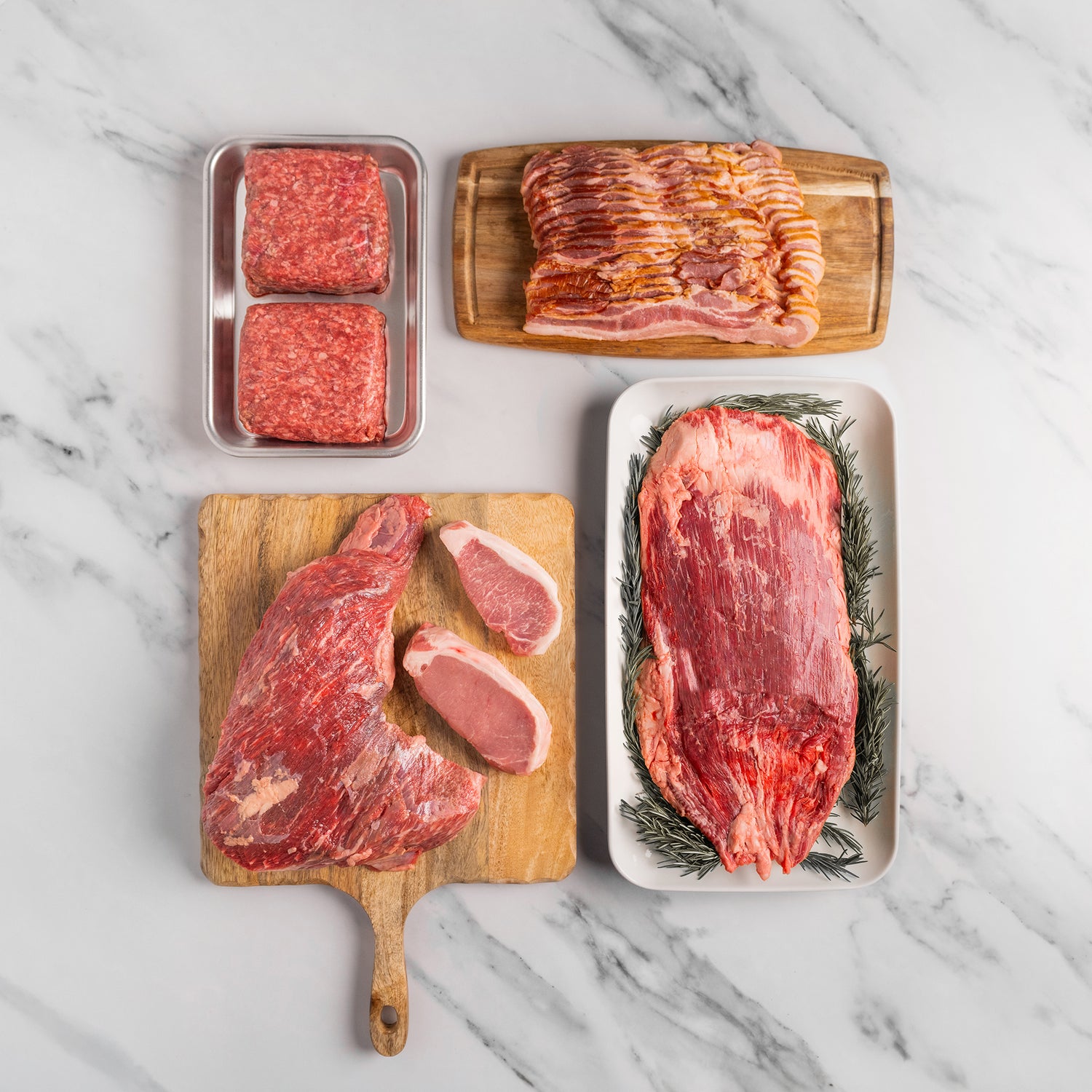 Assorted raw meats on a marble surface including steaks, bacon, and ground beef.