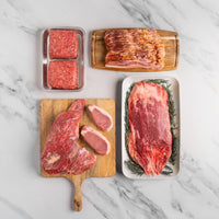 Assorted raw meats on a marble surface including steaks, bacon, and ground beef.