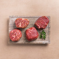 Four raw beef steaks on a stone cutting board with a leaf on a beige background