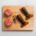 two wagyu ribeye filet steaks and two lobster tails on a cutting board on a white tile background