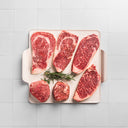 USDA Raw Prime steaks on a white dish on a white tile background