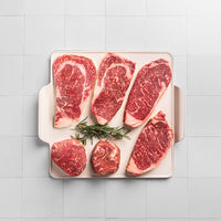 USDA Raw Prime steaks on a white dish on a white tile background