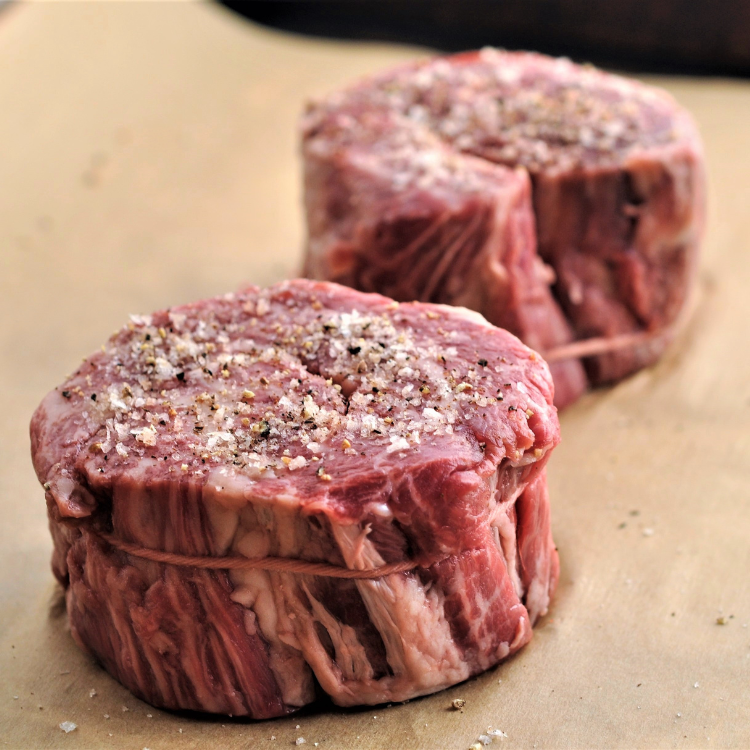two raw rolled cap of ribeye with seasoning and tied