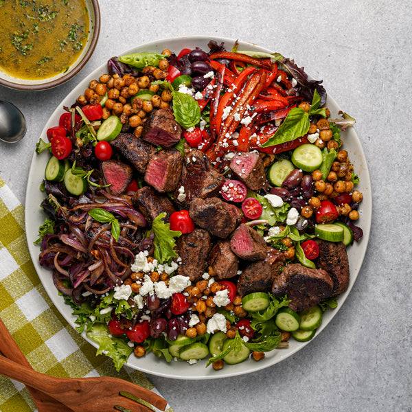 Platter of salad with meat, vegetables, and chickpeas on a gray surface.