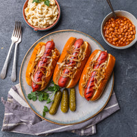 cooked hot dogs in buns with onions and side dishes 