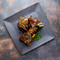 cooked short ribs on plate with sauce and parsley 