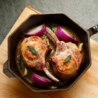 cooked Kurobuta pork chops in cast iron pan with red onion and sage leaves 