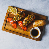 Two main tale lobsters on a cutting board with bread and lemon 