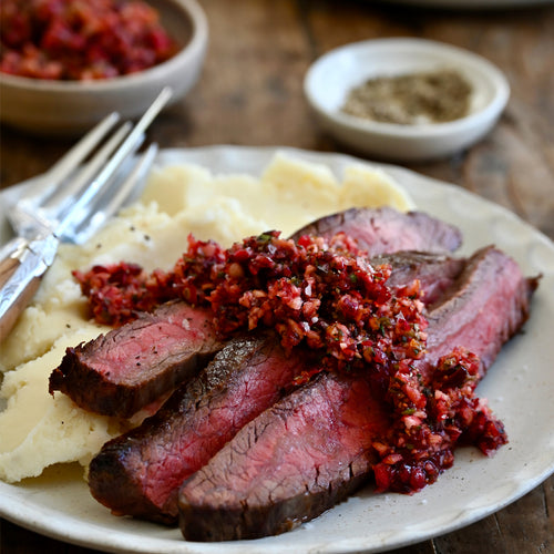 Sliced flank steak with cranberry compote on mashed potatoes with a wooden background
