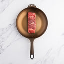 A single ribeye steak in a frying pan on a marble surface