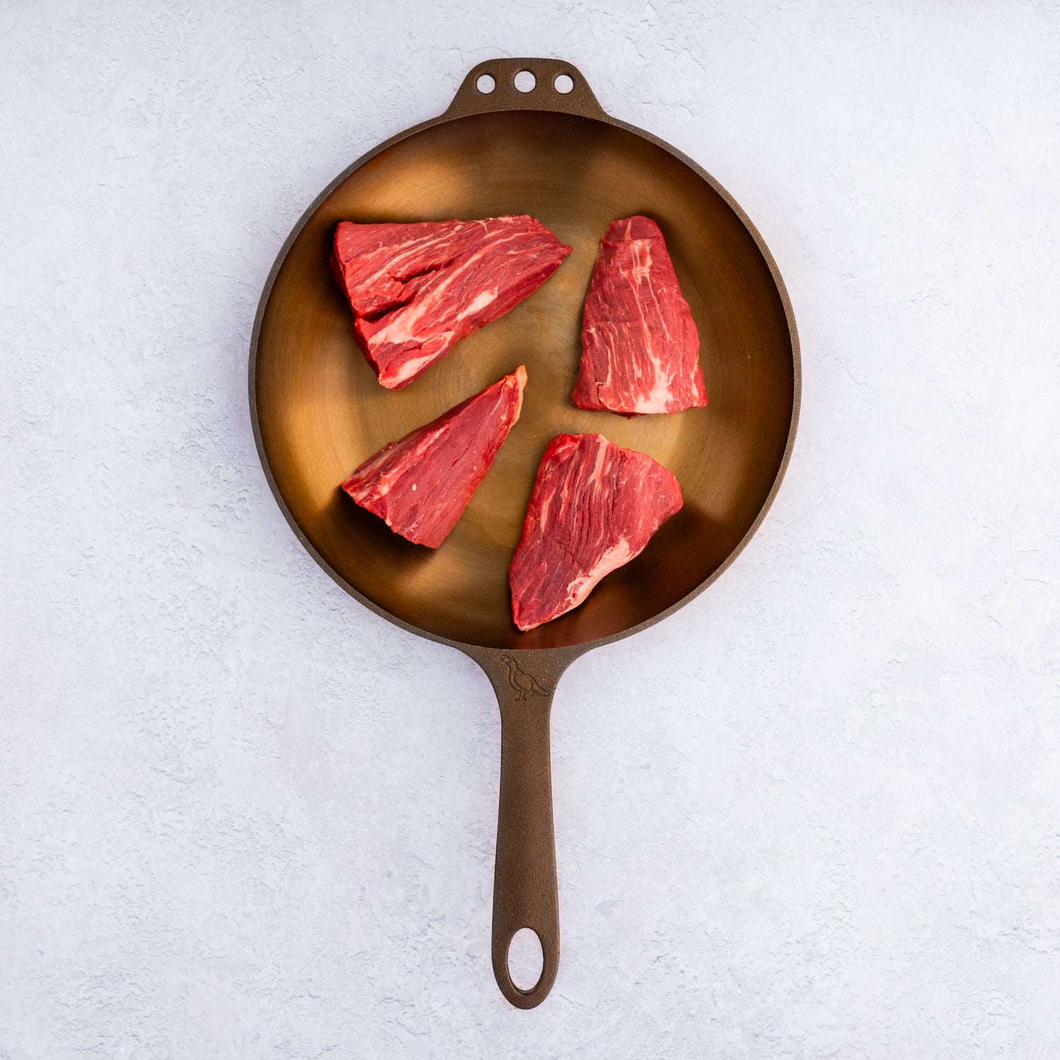 Raw filet mignon pieces in a skillet on a white background