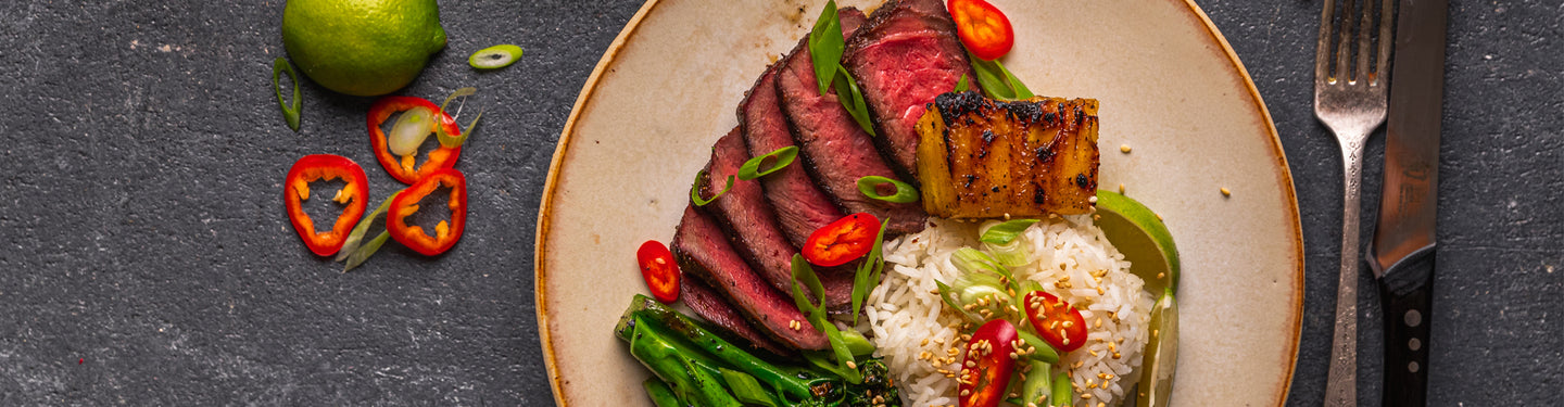 Steak dish with vegetables on a plate, garnished with herbs, on a dark surface.