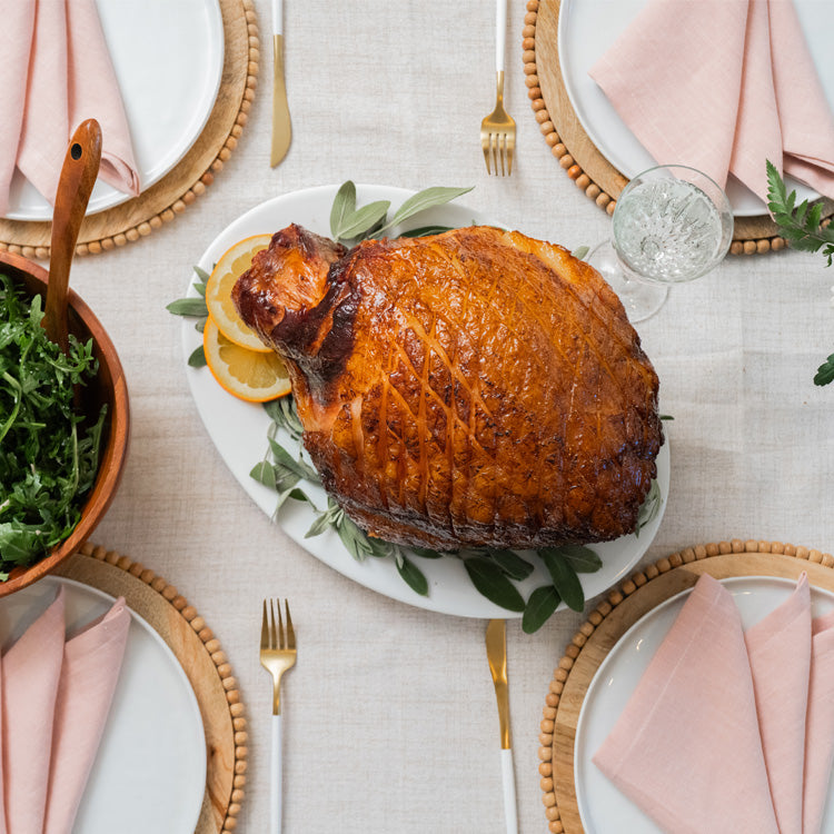 Roasted Kurobuta ham on a plate with garnishes on a festive table setting.