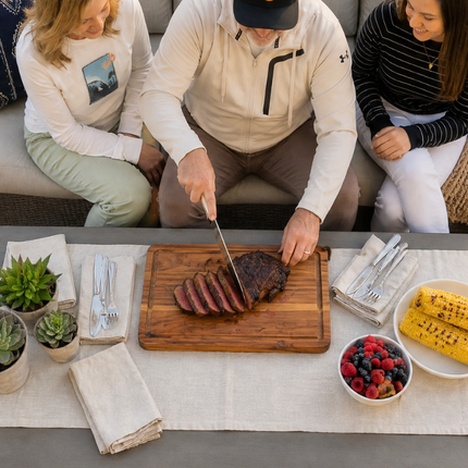 Ribeye Steak being sliced on a cutting board with corn and fruit in side dishes