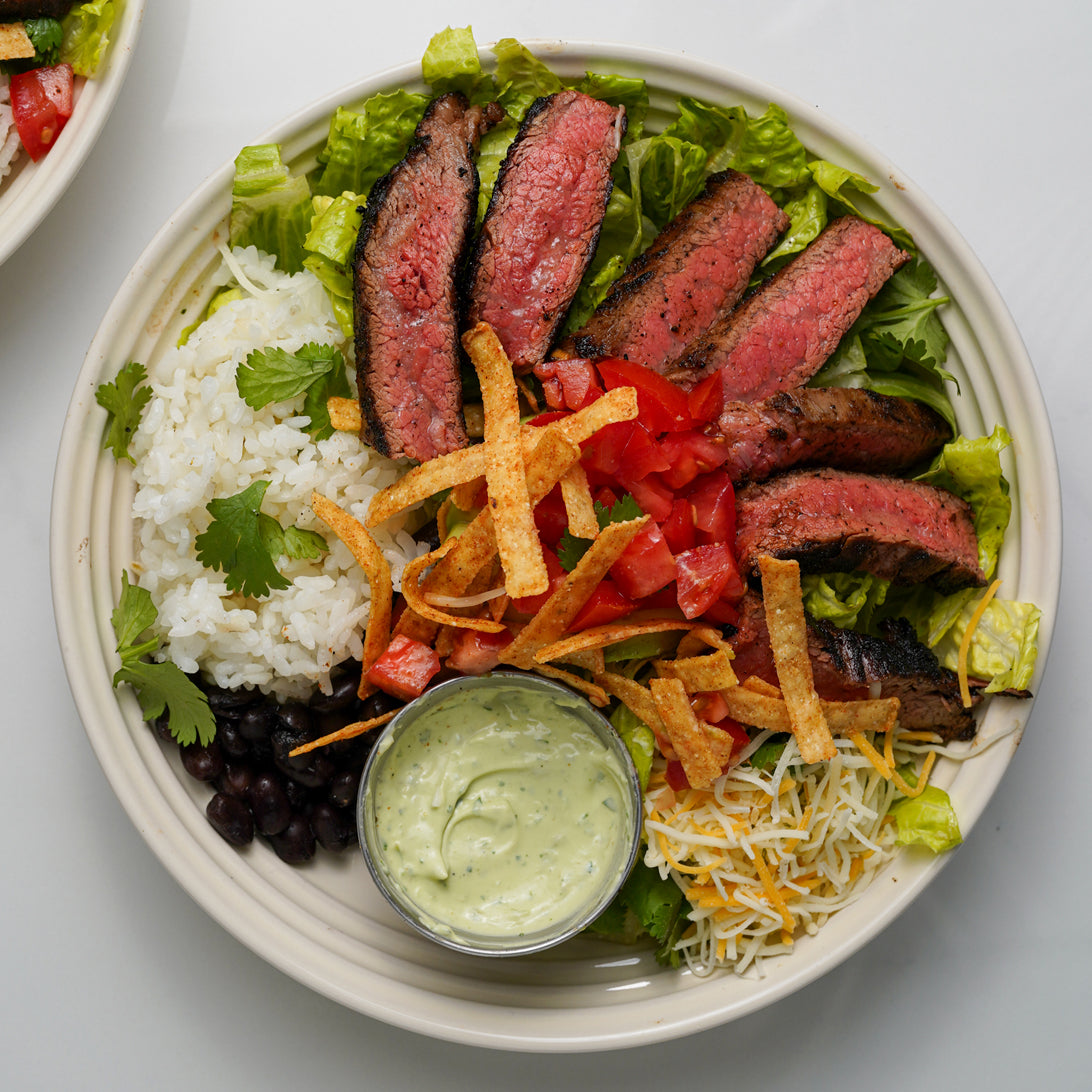 Plated dish with steak, rice, vegetables, and a side of guacamole on a white background