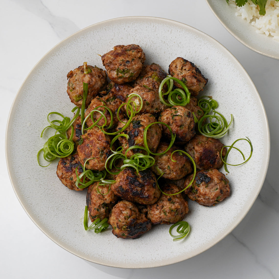 Platter of meatballs with green garnish on a white surface