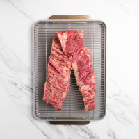 Raw outside skirt steaks on a metal grill rack over a white marble surface