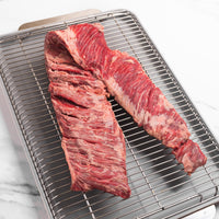 Raw skirt steak on a metal grill rack with a white background