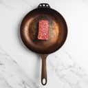 Raw steak on a cast iron skillet on a marble surface