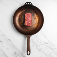 Raw steak on a cast iron skillet on a marble surface
